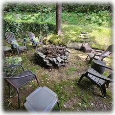 Large Stone Fire Pit Along Stream Surrounded By Furniture & Solar Lights